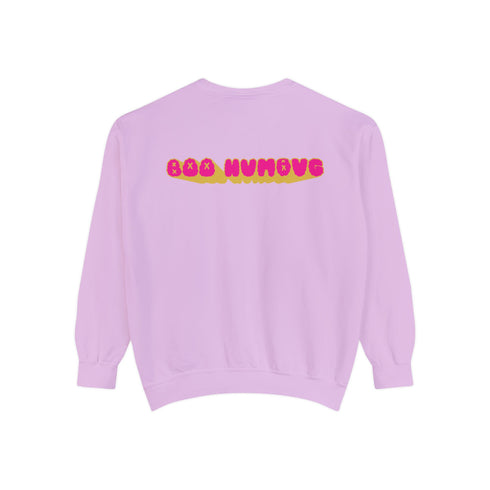 A holiday sweatshirt featuring a cute ghost character wearing a Santa hat, with two smaller ghosts on either side. Above them is the playful text "Boo Humbug," surrounded by snowflakes and festive elements. The design humorously combines spooky and festive themes for a unique holiday look.